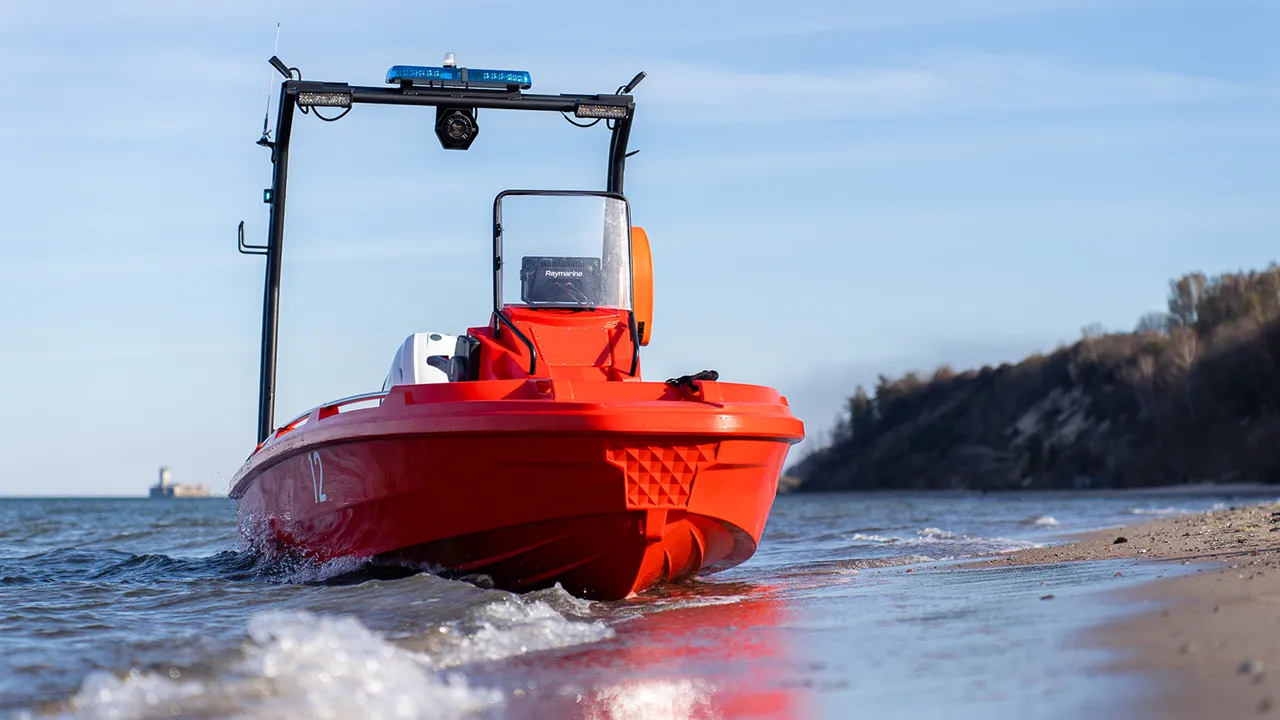 The Hydra 450 Rescue boat with a front console rests on the shore, with gentle waves and a distant coastline in the background.
