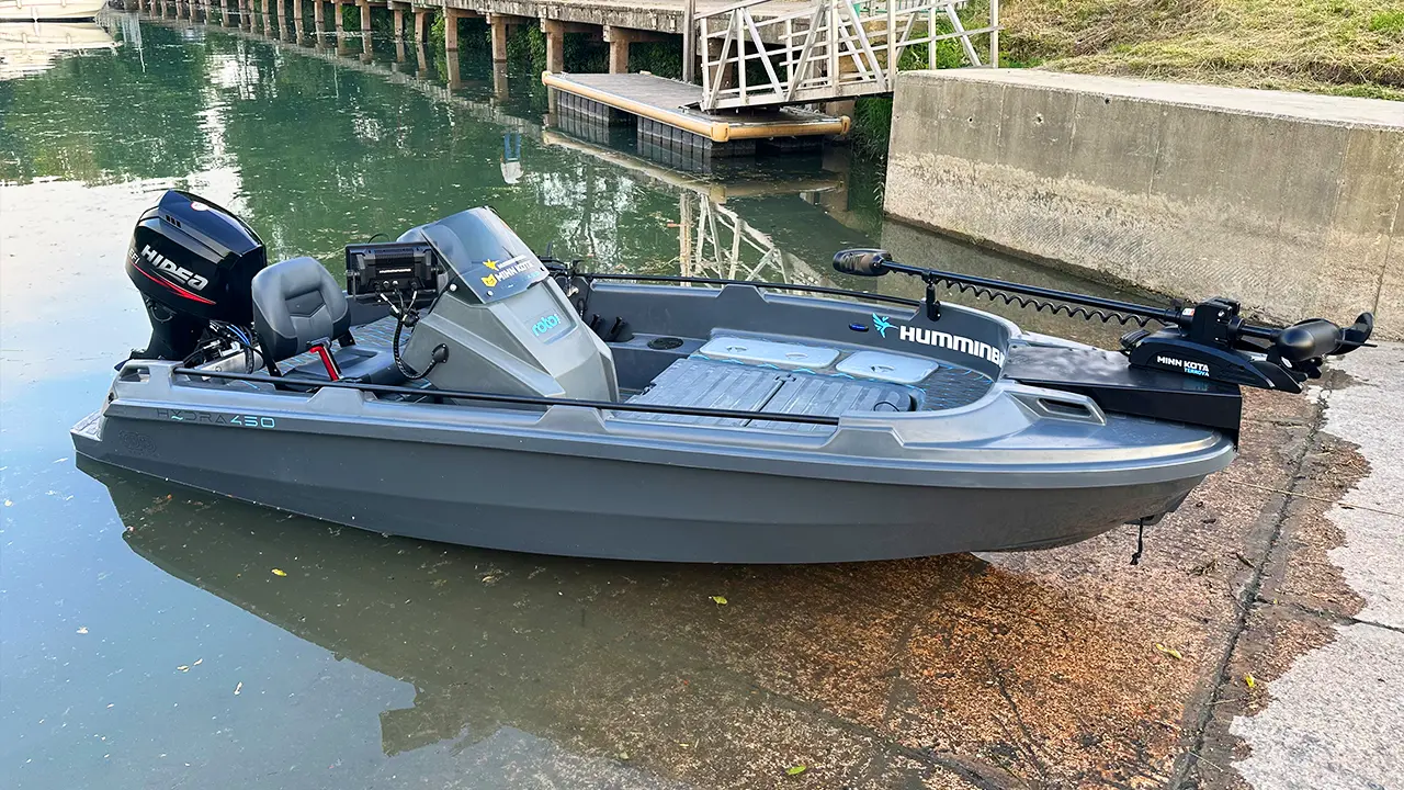 The Hydra 450 Fishing boat with a motor and trolling motor is docked by a concrete ramp on a calm waterway.