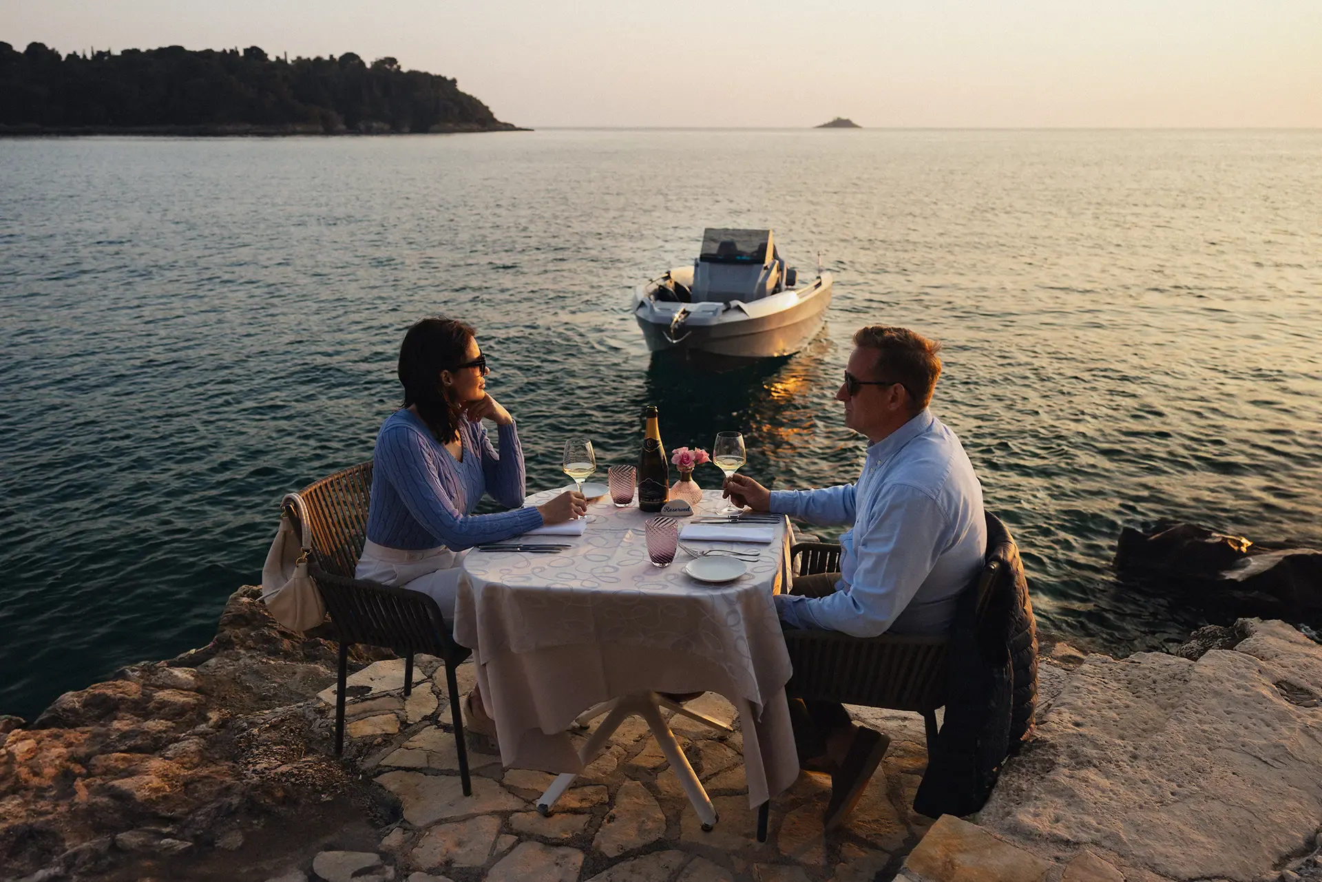 Una coppia che si gode una cena romantica al tramonto con la barca Hydra 530 Family sullo sfondo.