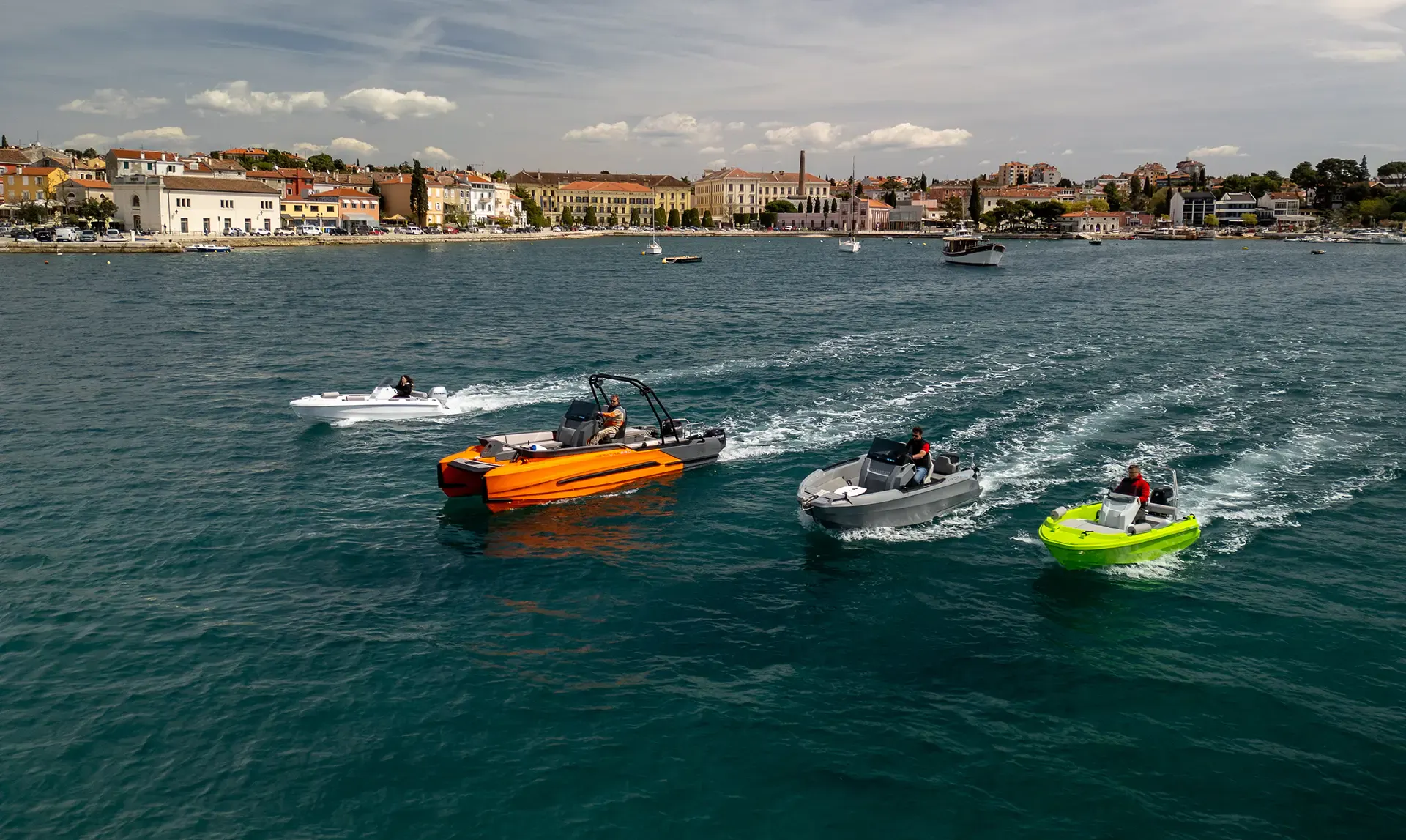 Four ROTO Nautica rotomolded boats speed across blue water near a coastal town.