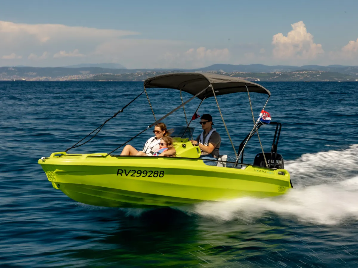 A lime-green Hydra 460 polyethylene best boat for beginners, cruising on the sea on a sunny day.
